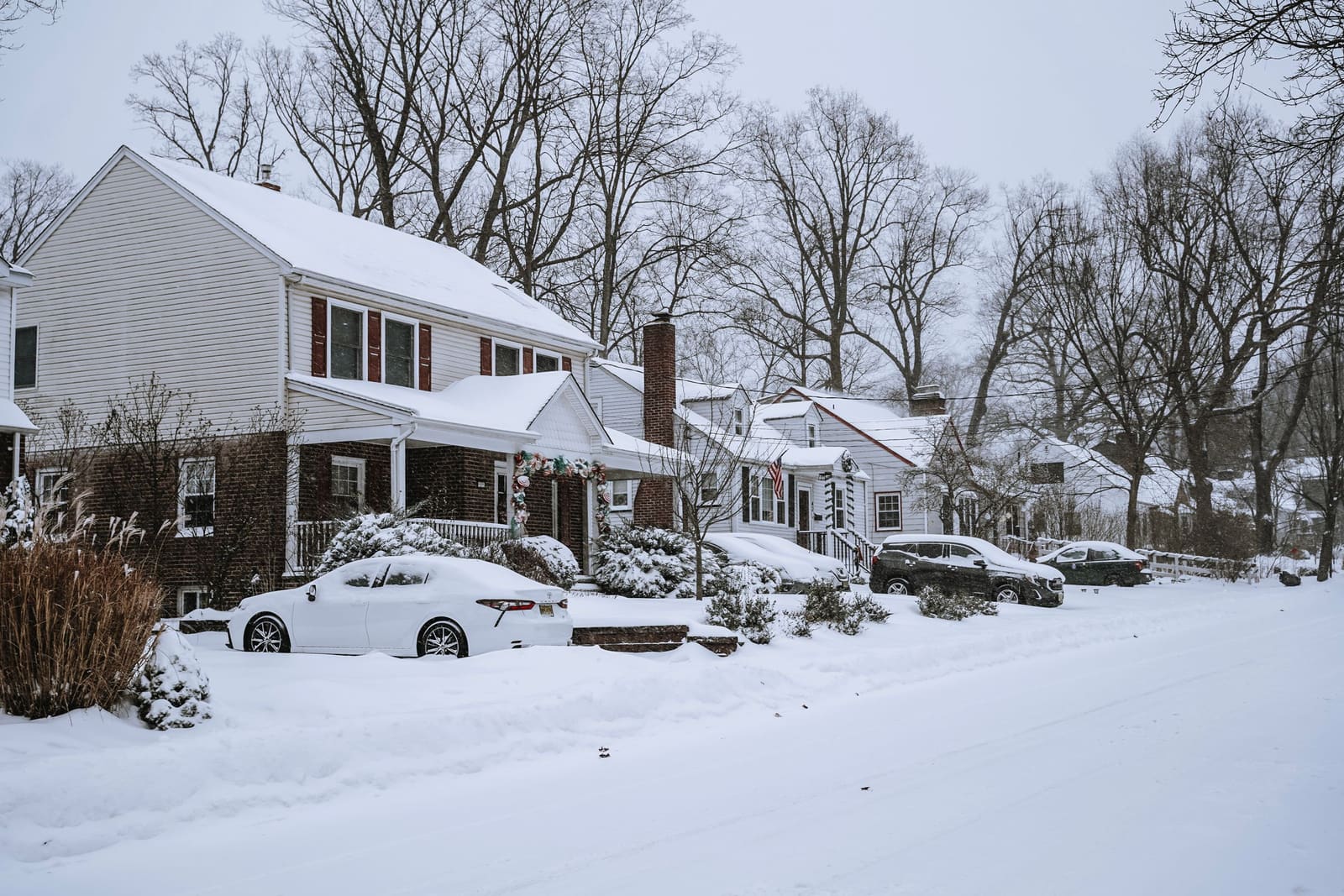 Snow-covered residential street lined with two-story houses and parked cars after a snowfall